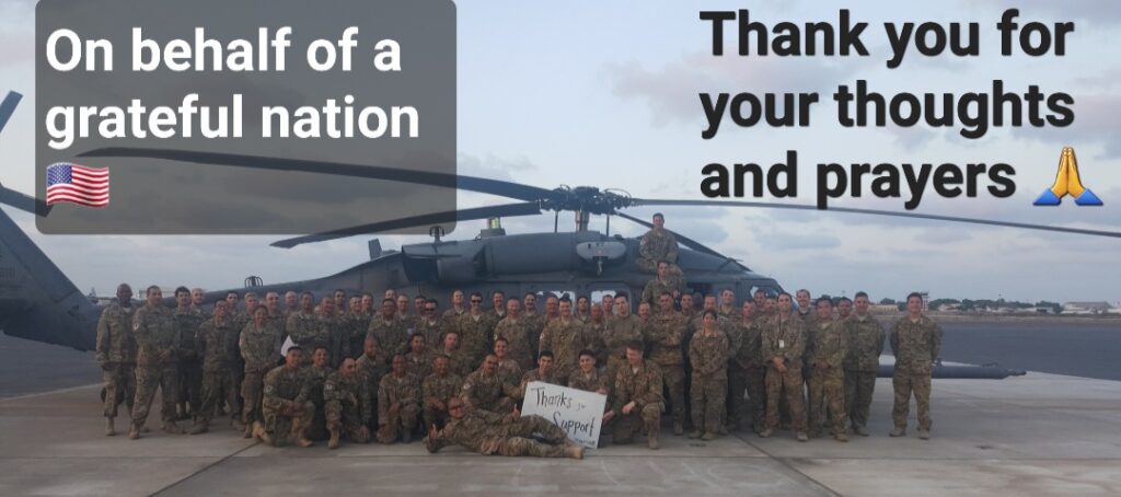 Deployed Unit of Service Members in front of a helicopter with a sign that says Thank You