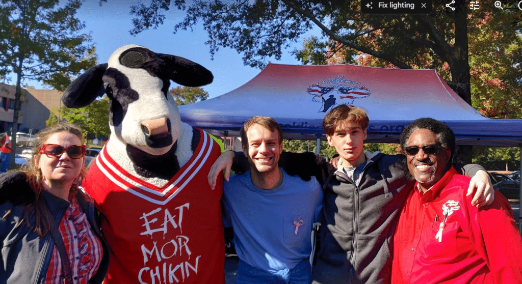 Four people smiling alongside the Chick-fil-A cow mascot at a Soldiers' Angels food assistance event