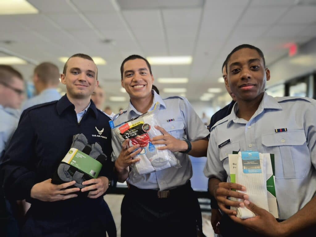 Three U.S. Air Force service members in uniform holding pairs of socks donated through the Warm Feet for Warriors program